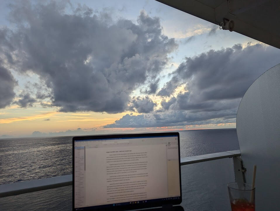 Writing by the Ocean A writer's laptop screen with a sun setting on open ocean behind it.